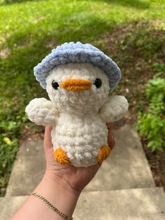 a hand holding a small crocheted white and blue stuffed animal with an orange beak