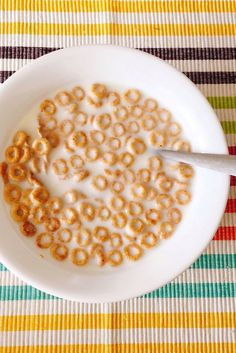 cereal in a bowl with milk being poured into it on a colorful tablecloth and striped place mat