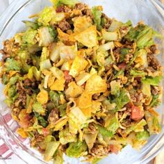 a glass bowl filled with lettuce and other food items on top of a wooden table