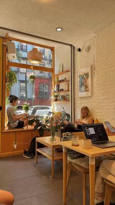 two people sitting at a table with laptops in front of them, looking out the window