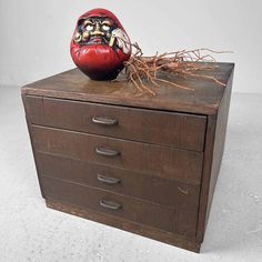 a wooden drawer with a red painted face on it's top and branches sticking out of the drawers