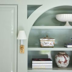 a green bookcase with books and vases on the shelves in front of it