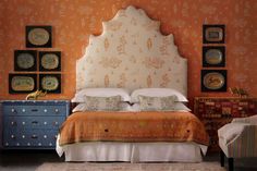 a bedroom with an orange wall and white bedspread on the bed, two chairs in front of it