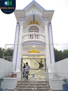 two men are painting the front of a white building with blue trimmings and gold decorations