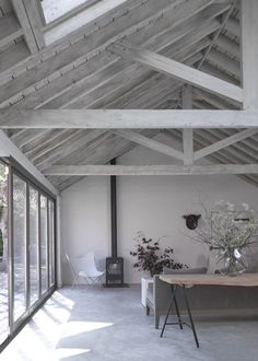 a room with white walls and wooden ceilinging has plants in vases on the table