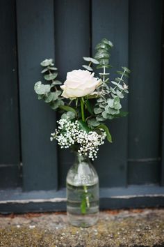 a white rose in a glass vase with baby's breath and greenery on the outside