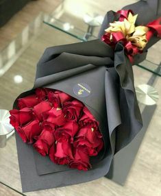 a bouquet of red roses sitting on top of a black box next to a glass table