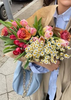 a woman holding a bouquet of flowers in her hand on the street with cars behind her