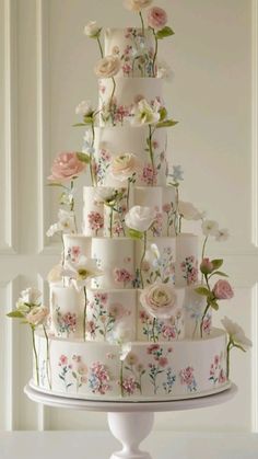 a wedding cake decorated with flowers and candles on a white tableclothed pedestal in front of a wall