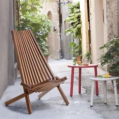 a wooden chair sitting on top of a sidewalk next to a table and potted plants