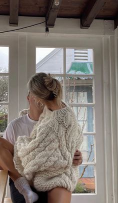 a woman is sitting on a window sill with her arms wrapped in a sweater