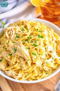 a white bowl filled with pasta and chicken on top of a wooden cutting board next to glasses