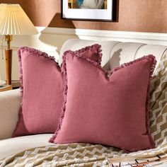 two pink pillows sitting on top of a white couch next to a lamp and pictures