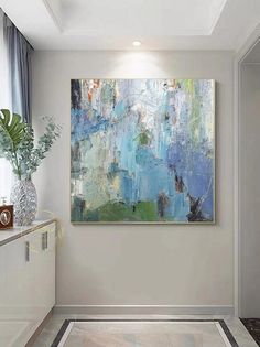 an abstract painting hangs on the wall in a white room with blue and green accents