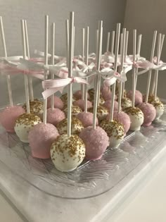 cake pops with pink and gold sprinkles are arranged on a clear platter