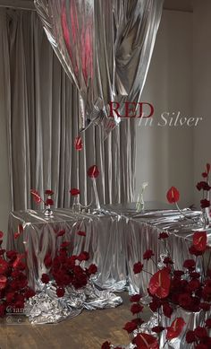 red flowers are placed in clear vases on the floor next to silver sheets and drapes