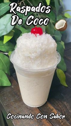 a plastic cup filled with ice cream and topped with a cherry sitting on top of a wooden table