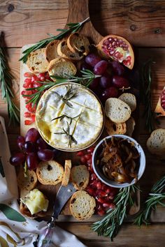 an assortment of cheeses, grapes and crackers on a cutting board with rosemary sprigs