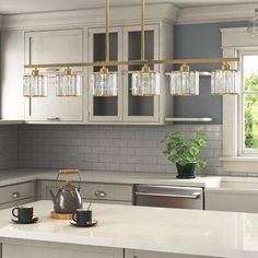 a kitchen with gray cabinets and white countertops has a kettle on the island in front of it