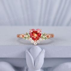 a pink heart shaped ring with two green leaves on the front and one red stone in the middle