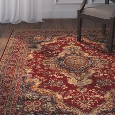 a red area rug with an ornate design on the center and bottom, in front of a window