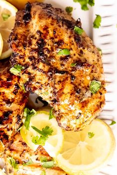 grilled chicken with lemons and parsley on a white plate next to sliced lemons