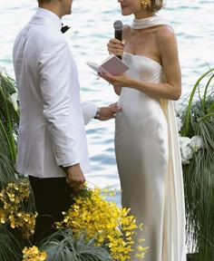 a man and woman standing next to each other in front of flowers holding a microphone