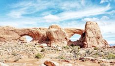 an arch in the desert with rocks and plants around it, under a blue sky