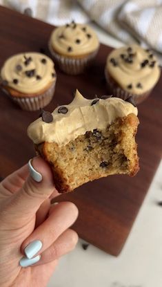 a hand holding a half eaten cupcake with frosting and chocolate chips on top