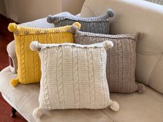 three pillows on a couch with pom - poms in different colors and sizes