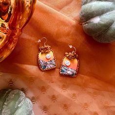 A pair of handmade arch-shaped earrings with a hand-sculpted golden frame and a mountain sunset landscape. Earring bases are silver, apply as dangles, and are nickel free and hypoallergenic. (Please read shop policies before purchasing). Polymer Clay Landscape, Clay Landscape, Landscape Earrings, Mountain Sunset Landscapes, Golden Frame, Mountain Sunset, Sunset Landscape, Jewelry Inspo, Shop Policies