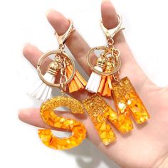 a pair of orange and white earrings sitting on top of a persons hand in front of a white background