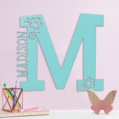 the letter m is made up of wood and has flowers, butterflies, and hearts on it