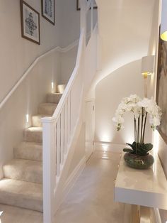 there is a vase with white flowers on the table next to the stairs in this house