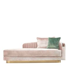 a pink couch with green pillows and a gold frame on the bottom, in front of a white wall