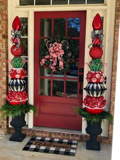 two christmas decorations on top of planters in front of a red door with black and white checkered mat