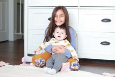 a woman sitting on the floor holding a baby in her lap and smiling at the camera