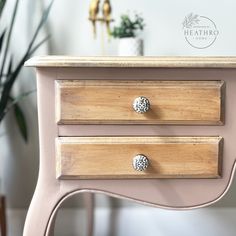 a pink dresser with three drawers and two knobs on the bottom drawer, next to a potted plant