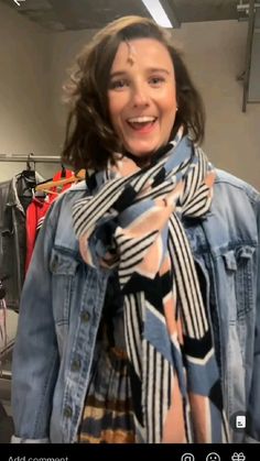 a woman wearing a jean jacket and scarf in a room with clothes on hangers