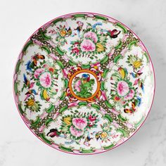 a decorative plate with flowers and birds painted on the side, sitting on a marble surface