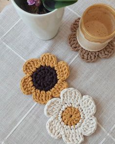 three crocheted coasters sitting on top of a table next to a cup of coffee