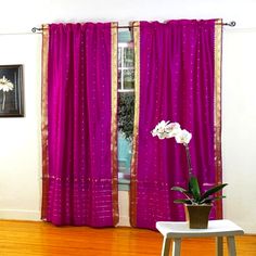 a living room with wooden floors and purple drapes on the windowsill, along with a potted plant