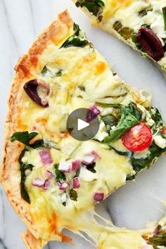 a pizza with spinach, cheese and tomatoes on it sitting on a marble surface