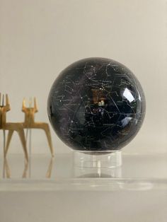 a black marble ball sitting on top of a table next to two gold figurines