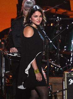 a woman standing in front of a microphone on top of a stage with other musicians behind her