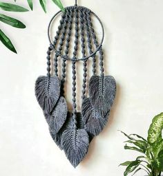 a wall hanging with beads and feathers on it next to a potted green plant