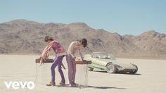 two people standing next to a car in the desert