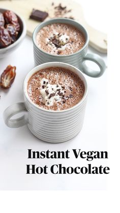 two mugs filled with hot chocolate on top of a white table next to nuts