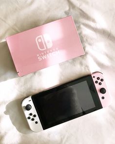 a nintendo switch sitting on top of a bed next to a pink box