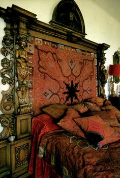 a bed with an ornate headboard and red bedspread on top of it